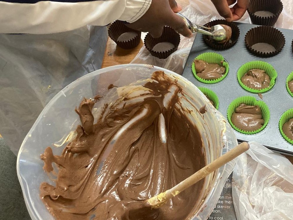 A bowl of chocolate cake mixture beside a filled muffin tin