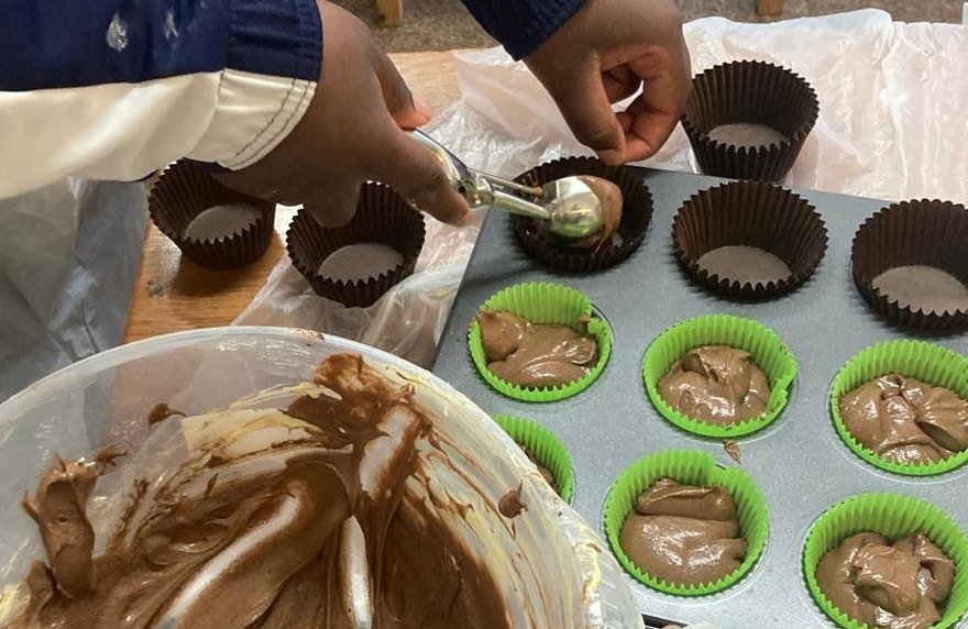 Spooning chocolate cake mixture into paper cases in a muffin tin
