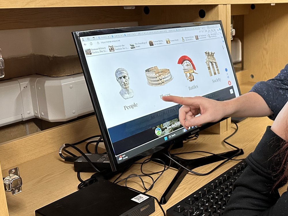 A member of staff pointing at a screen while a student works at a computer