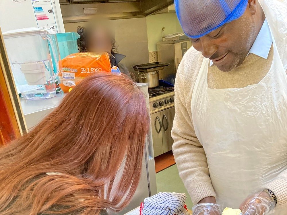 A member of staff and a student making cakes together in the school kitchen, weighing out butter in aprons and gloves