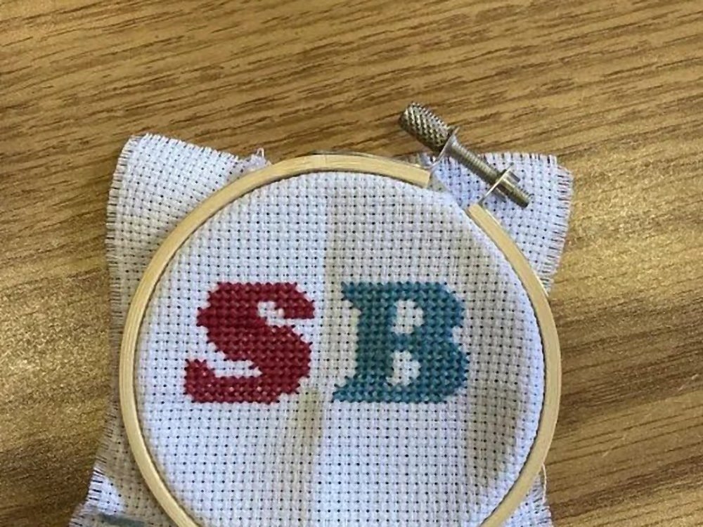 A finished cross-stitch of the initials S and B in an embroidery hoop