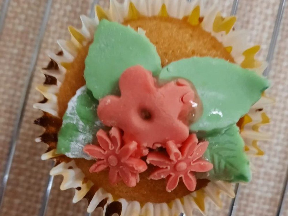 A fairy cake decorated with icing flowers and leaves on a cooling rack