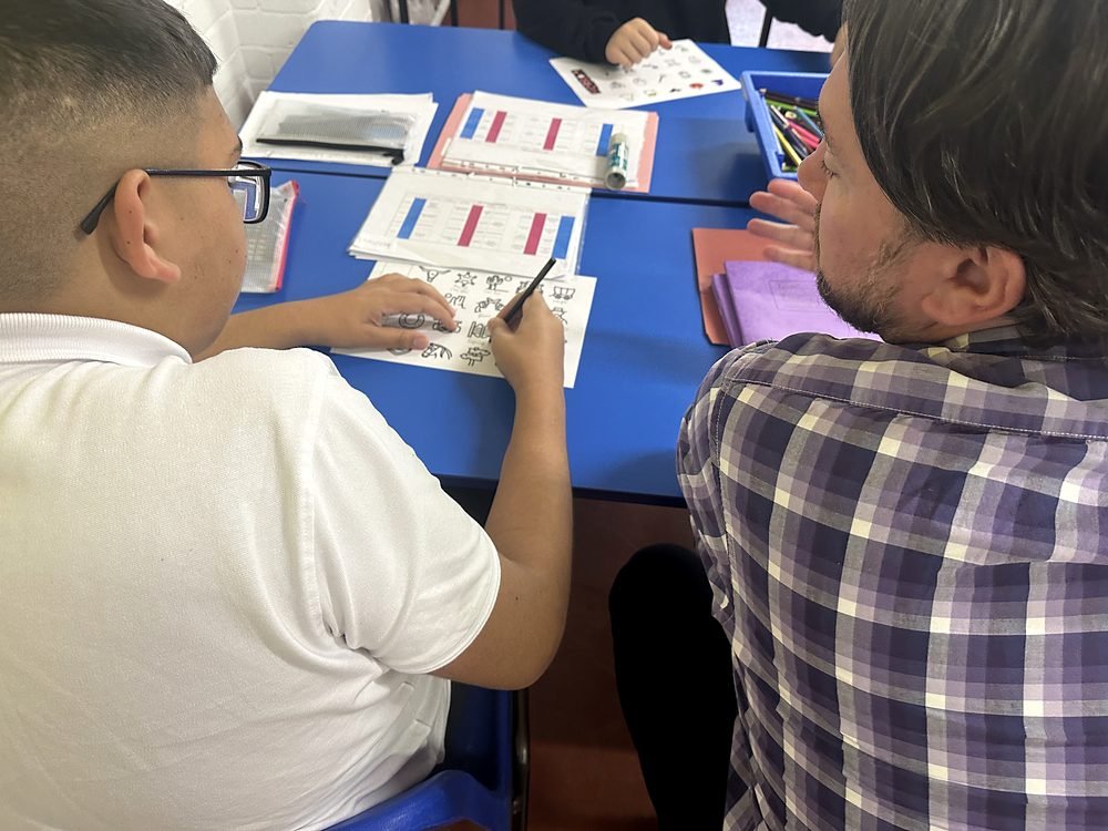 A teacher working one to one with a student on an English vocabulary worksheet, labelling pictures with the words that match