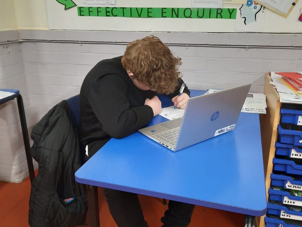 A student working independently at a laptop beneath an Effective Enquiry display