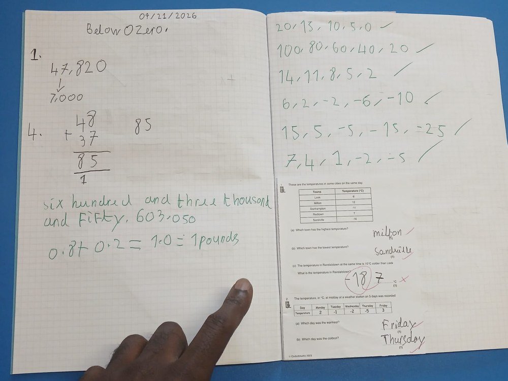 An open exercise book showing work on negative numbers, with a member of staff pointing at the page