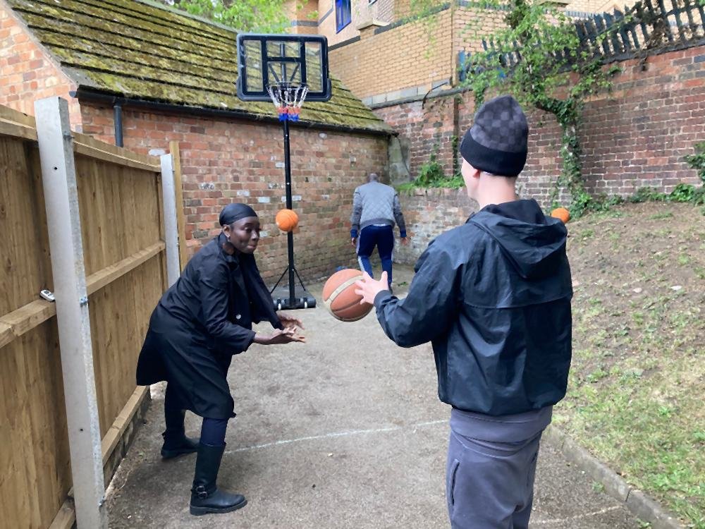 A member of staff passing a basketball to a student on the court outside school, with the hoop behind them