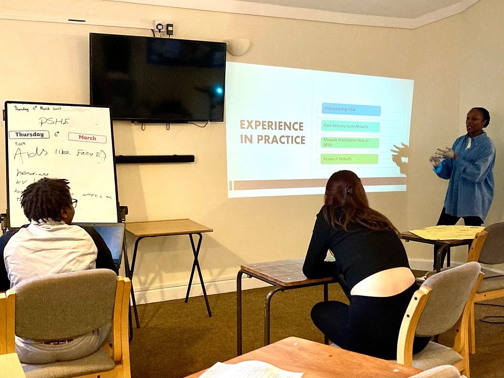 A visiting midwife giving a careers talk to students in a PSHE lesson, with her slides projected on the wall