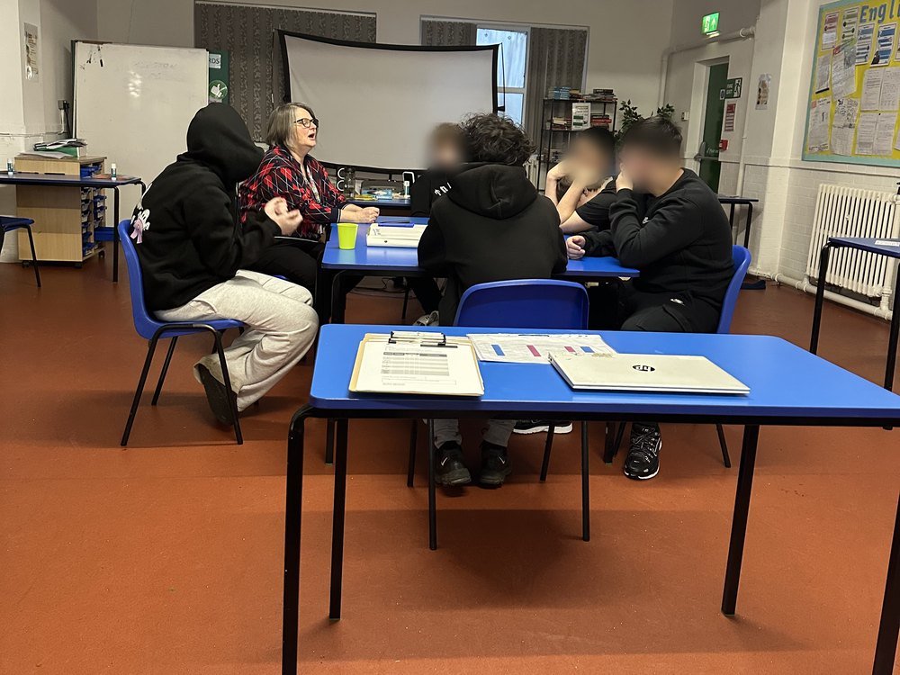 A visiting speaker leading a small group discussion around a table, student faces obscured